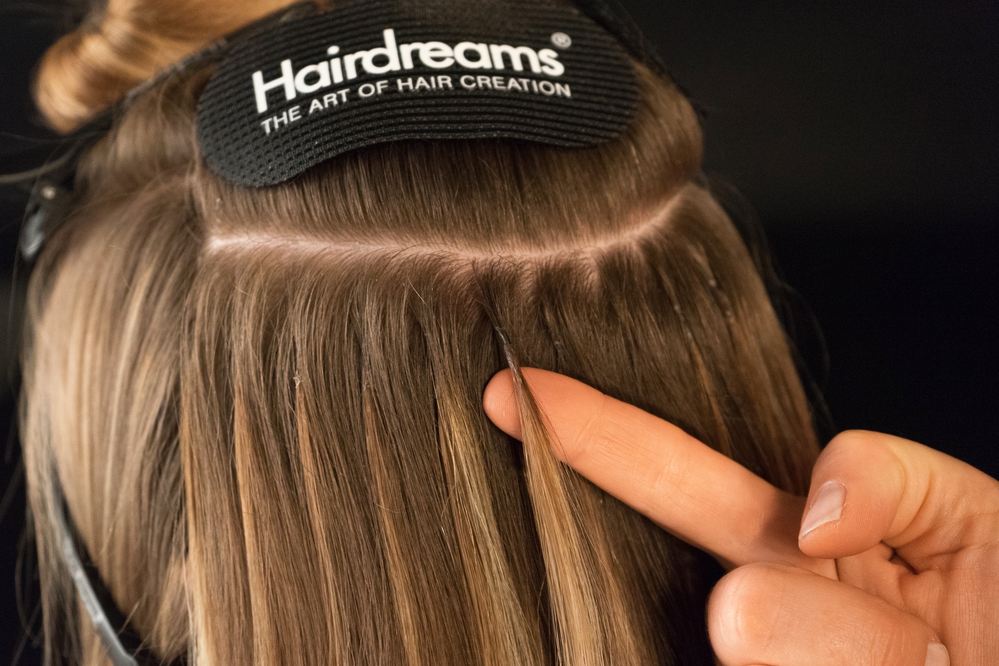 Eine Hairdreams-Friseurin zeigt die Gleichmäßigkeit einer Haarverdichtung mit Bonding-Extensions.